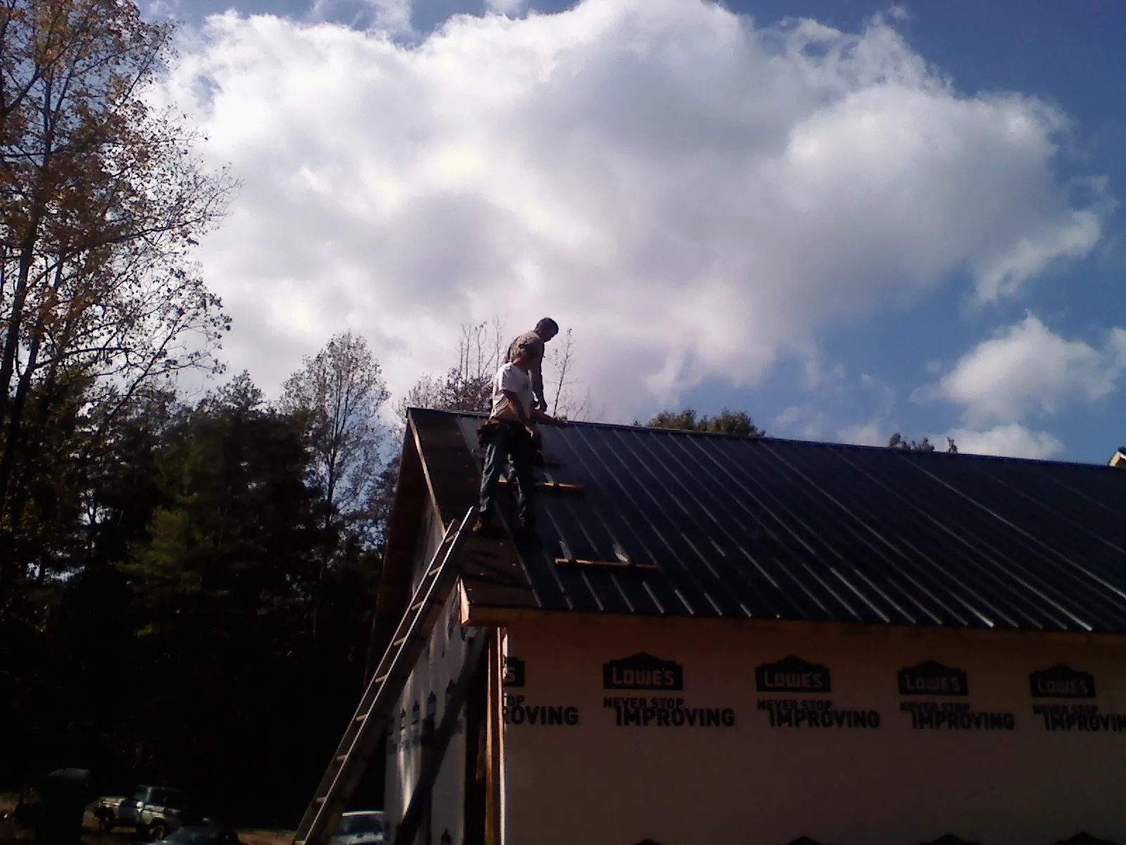 Roofer fastening dark metal panels high against a cloudy sky, from a Roof Inspection job in Grapeview